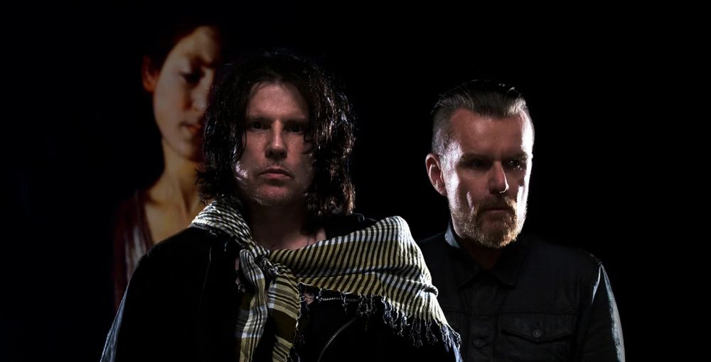 The Cult, fot. materiały prasowe Dwóch mężczyzn na tle czarngo ekranu z wizerunkiem zamyślonej kobiety.