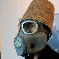 Mężczyzna w masce gazowej i wiklinowym koszu na głowie.