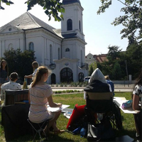 Latu. Uczestnicy kursu widziani z tyłu w plenerze szkicują kosciół Wszystkich Świetych na Grobli w w Poznaniu.