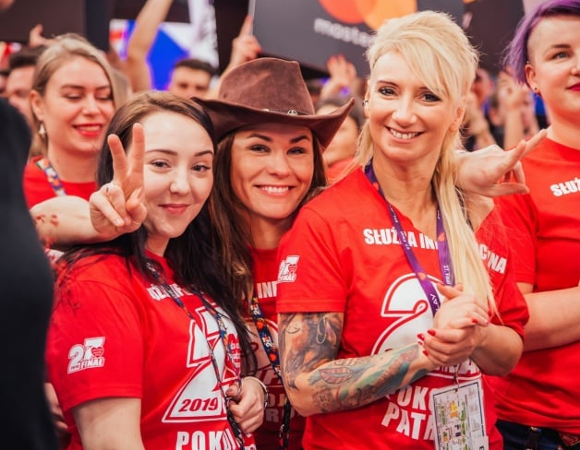 Grupa dziewczyn w czerwonych koszulkach służby informacyjnej WOŚP uśmiecha się do obiektywu.