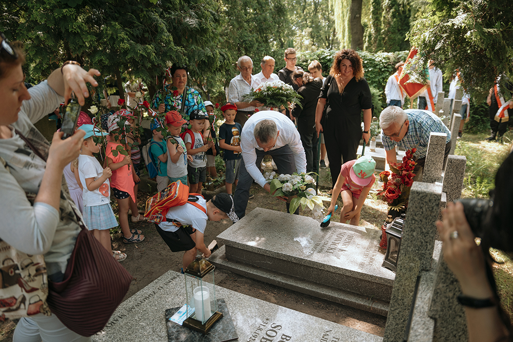 Dzieci, rodzice i z-ca Prezydenta J. Solarski składają kwiaty ma nagrobie.