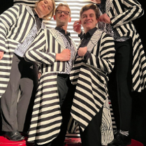 Zdjęcie aktorów - kobieta i trzech mężczyzn we frakach w biało-czarne paski.