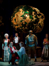 Na scenie aktorzy w kostiumach z epoki, na pierwszym planie klęczą mężczyzna i kobieta, za nimi rząd innych postaci. Wszyscy śpiewają.