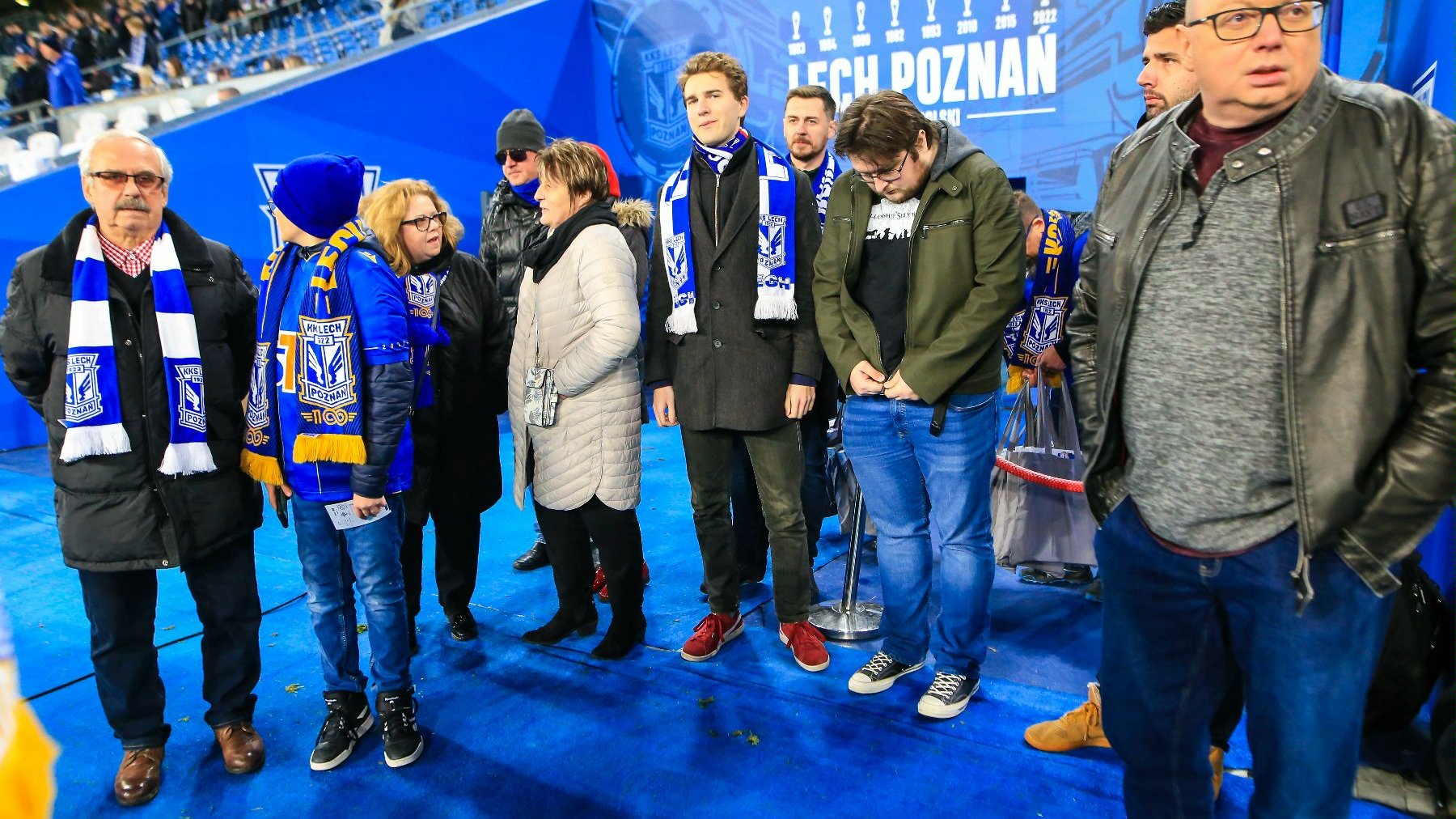 Laureaci konkursu "W górę serca" na stadionie Leche Poznań. Na zdjęciu jest kilkanaście osób odbierających dyplomy i nagrody. Wszyscy stoją na murawie i mają szaliki Kolejorza.