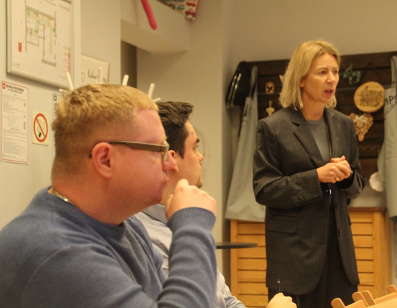 Ludzie siedzą przy stole i słuchają osoby prowadzącej warszaty