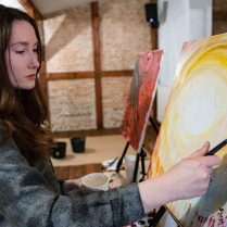 Zdjęcie, kobieta stoi przed sztalugą i maluje obraz