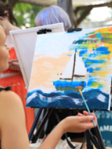 Osoba maluje obraz na sztaludze farbami akrylowymi.