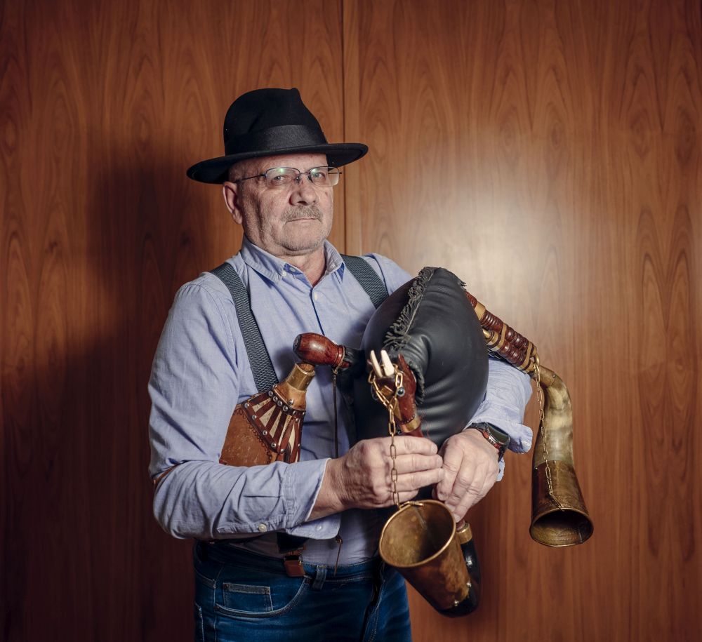 Mężczyzna siedzi na krześle, trzymając pewnie dudy, fotograf stoi nad nim.