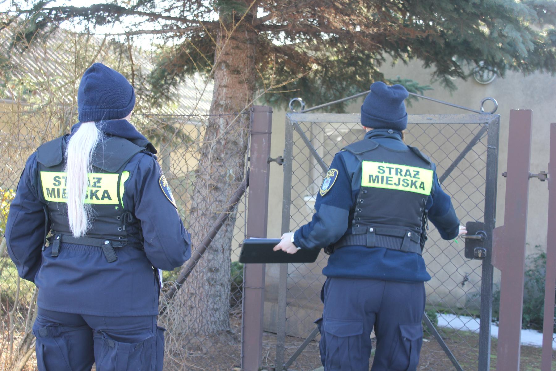 Na zdjęciu dwie strażniczki miejskie, przed domem jednorodzinnym, aura zimowa