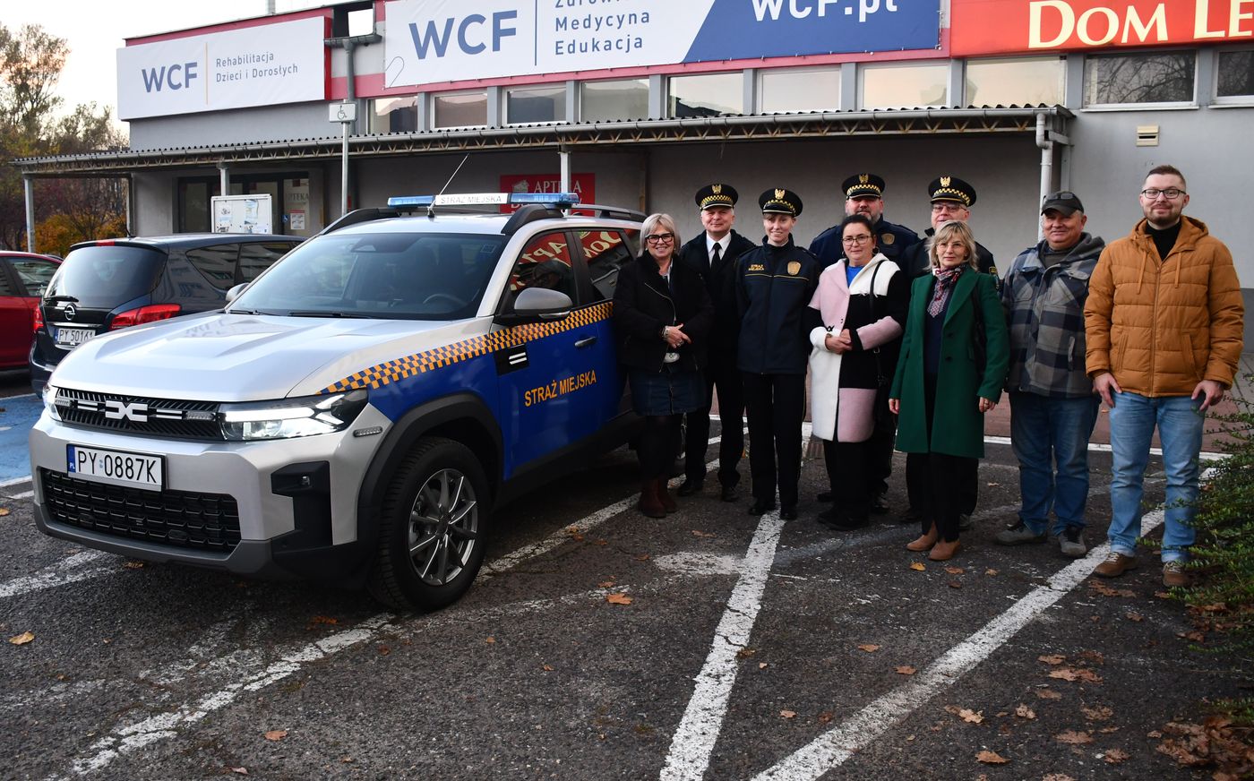 na zdjęciu dziewięć osób stoi na parkingu przy radiowozie, strażnicy miejscy w mundurach oraz przedstawiciele rad osiedli