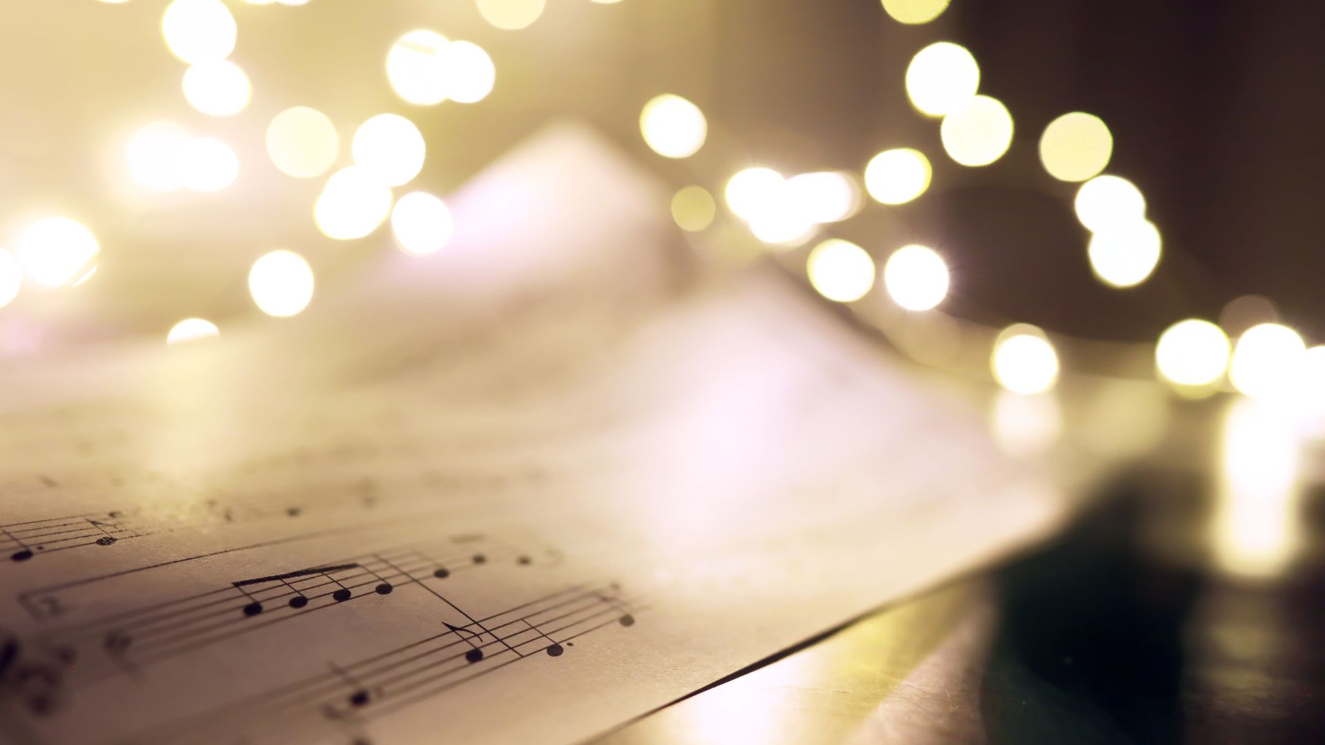 Na zdjęciu widać zapis nutowy oraz lampki świąteczne w ciepłym kolorze