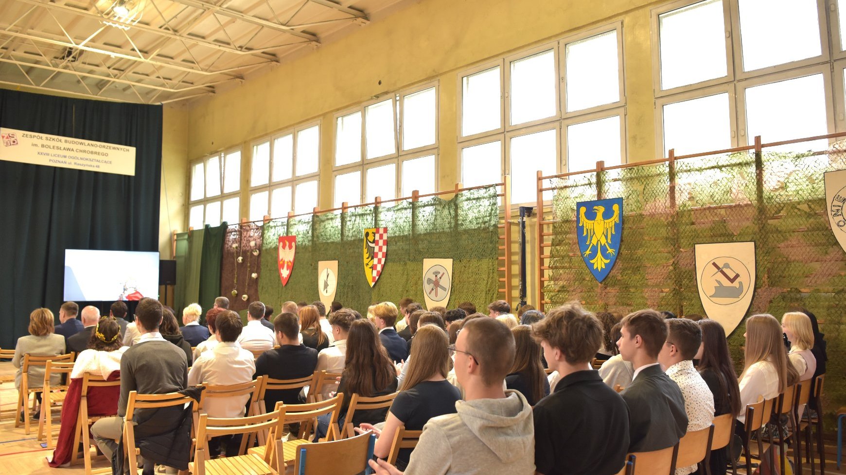 Zdjęcie przedstawia uczniów siedzących na sali gimnastycznej.
