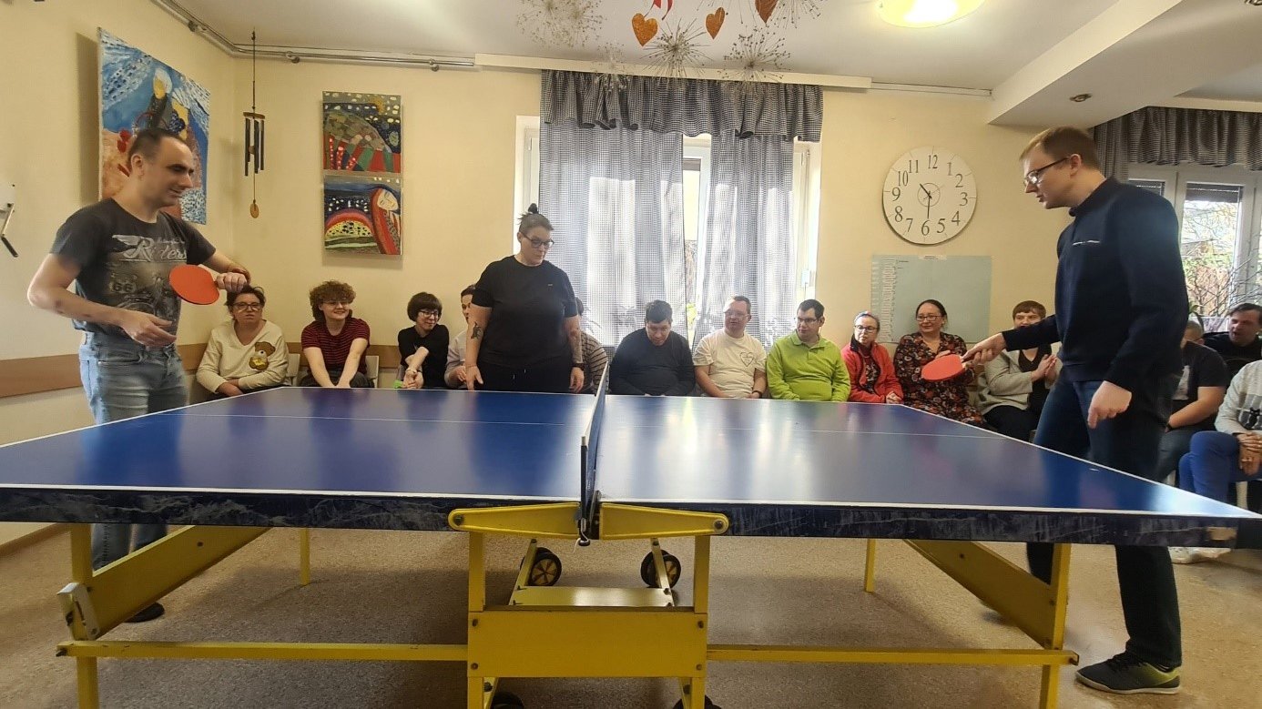 Dwóch mężczyzn przy stole do gry w tenisa stołowego, w tle grupa kibiców
