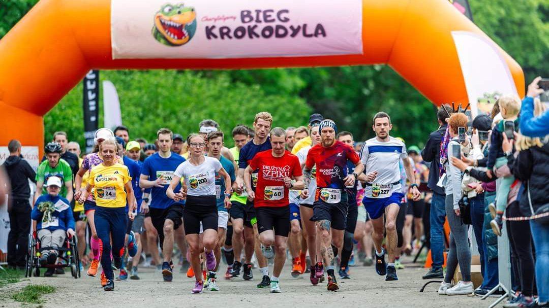Bieg Krokodyla 2024 - kilkadziesiąt osób rozpoczyna start biegu. W tle widać pomarańczową bramę pneumatyczną, a z boku dopingujących kibiców