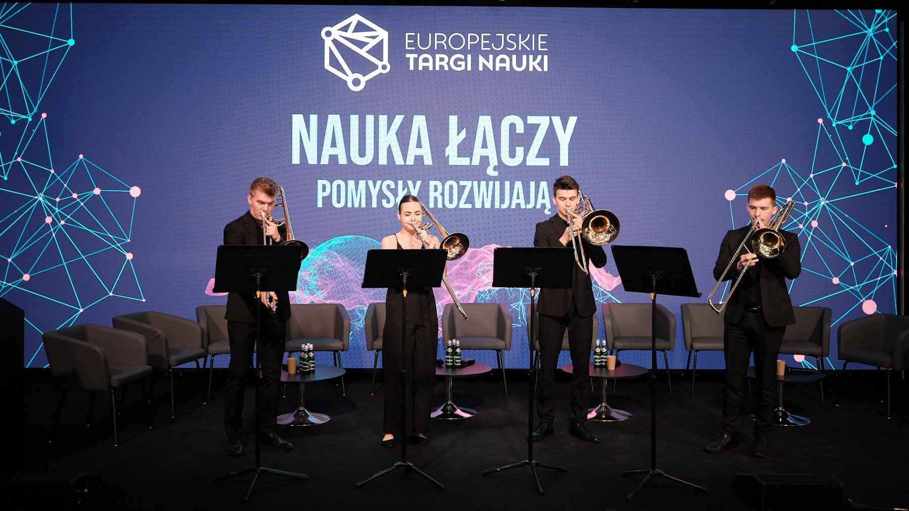 Zdjęcie przedstawia czworo muzyków grających na puzonach na scenie