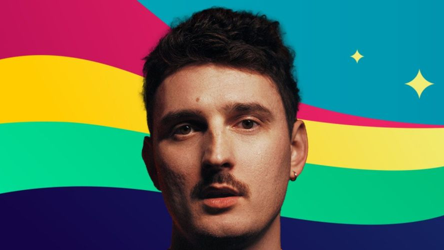 Dawid Podsiadło z kolczykiem w uchu i zmierzwionymi włosami patrzy prosto w obiektyw. Za nim tęczowe tło i dwie gwiazdki.