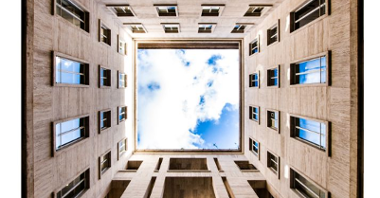 Fotografujący patrzy w górę, stoi idealnie w tym miejscu, w którym widać przeszklony sufit budynku, pokazujący błękitne, pogodne, pełne chmur niebo. Pod sufitem widać cztery ściany.
