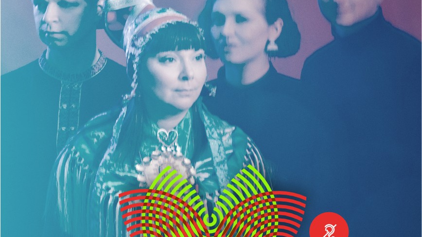 Śpiewaczka ma długie czarne włosy, zielony haftowany kostium oraz czerwony islandzki kapelusz. Za nią trójka osób z jej zespołu.