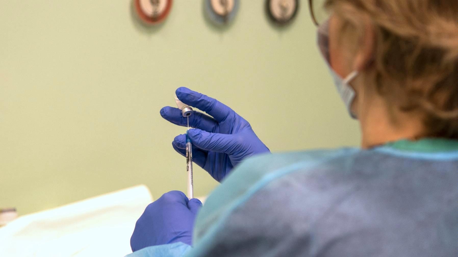 Na zdjęciu kobieta przygotowująca szczepionkę, w centrum jej dłonie i strzykawka - grafika artykułu