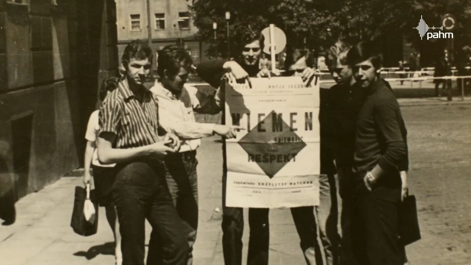 Kadr z filmu dotyczącego jubileuszu III Liceum Ogólnokształcącego. Przedstawia młodych ludzi trzymających plakat o koncercie Czesława Niemena. - grafika artykułu