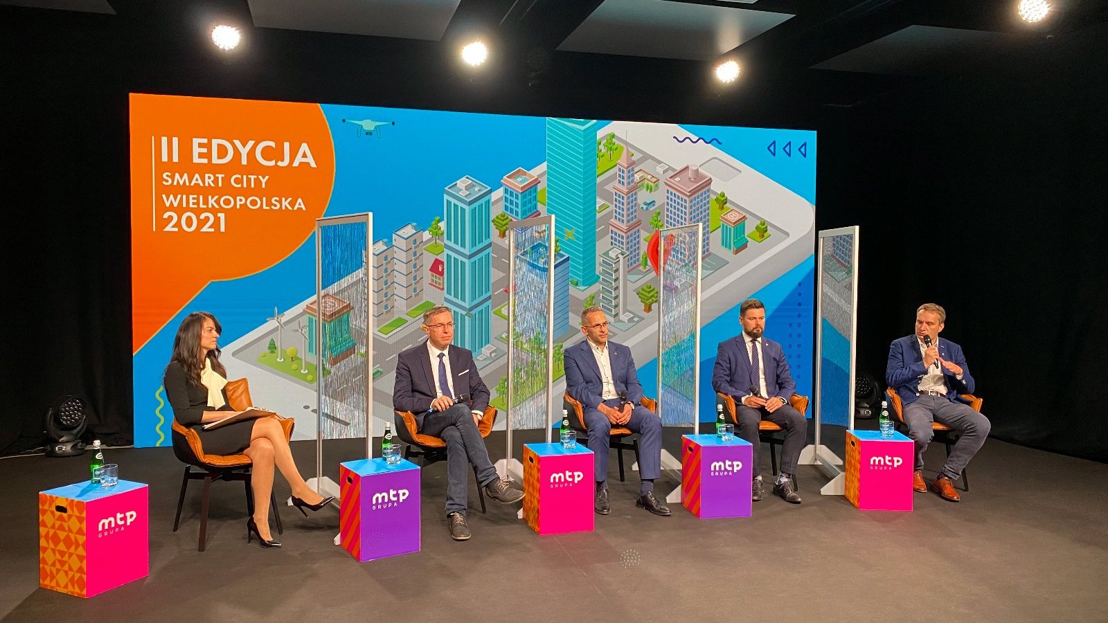 Zdjęcie z debaty prezydenckiej - pięć siedzących osób. Od lewej kobieta i czterech mężczyzn. W tle kolorowa grafika promująca wydarzenie. - grafika artykułu
