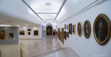 Wnętrze dużej sali wystawowej z obrazami na białych ścianach