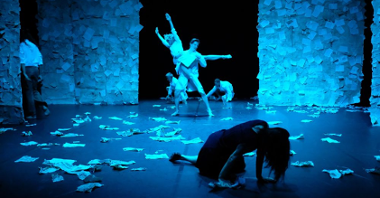 Zdjęcie w nebiesko-czarnych kolorach. Para tancerzy w tanecznej pozie na środku, przed nimi klęcząca i opierająca się o podłogę kobieta, za nimi dwie postacie. Na podłodze porozrzucane kartki papieru.