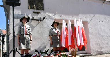Tablica pamięci Petera Mansfelda, po obu stronach harcerki, obok polskie flagi, pod tablicą kwiaty