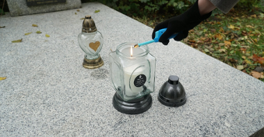 Zdjęcie rękę w rękawiczce zapalającą znicz stojący na grobie.