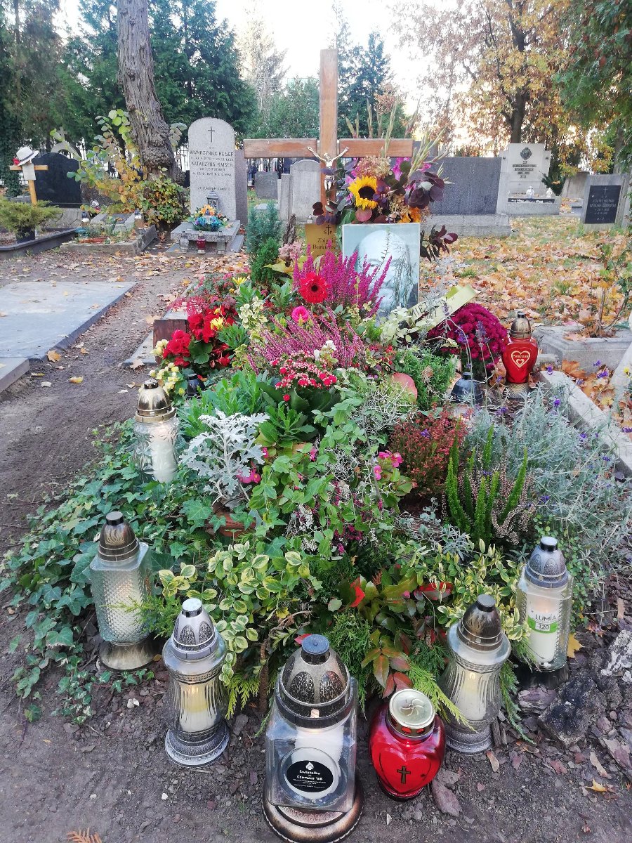 Zdjęcie przedstawia grób, na którym złożono kwiaty i zapalono znicze. - grafika artykułu