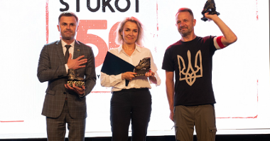 Na zdjęciu laureaci nagrody: dwaj mężczyźni i kobieta, wszyscy trzymają w rękach statuetki, w tle ekran z napisem Stukot '56
