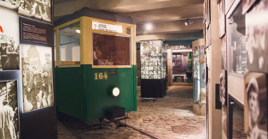 Część ekspozycji muzealnej Poznańskiego Czerwca 1956. W centrum stoi stary, żółto-zielony tramwaj z tablicą "2 Jeżyce. Ogród Botaniczny". Wokół tramwaju stoją filary ze zdjęciami z Poznańskiego Czerwca.