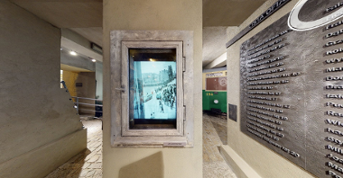 Element wystawy muzealnej, który przedstawia okno Paprzyckiego. W ramie okna kamienicy jest powieszon monitor, który wyświetla zdjęcia Leszka Paprzyckiego.
