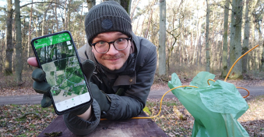 Na zdjęciu mężczyzna w lesie trzyma telefon w ręce.