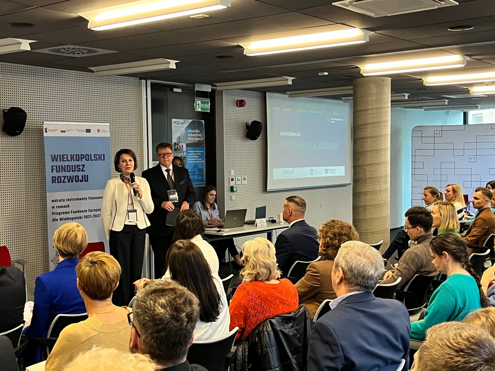 Finanse dla biznesu Otwarcie konferencji "Finanse dla biznesu" podczas Dni Przedsiębiorczości Poznań 2024. Dyrektor Wydziału Działalności Gospodarczej i Rolnictwa Joanna Jajus przemawia przez mikrofon, obok stoi Prezes Wielkopolskiego Funduszu Rozwoju Wojciech Marcinkiewicz. Stoją przed audytorium na tle banerów Wielkopolskiego Funduszu Rozwoju, Poznań Biznes Partner oraz Plus Jeden, w którym wydarzenie się odbywa.