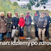 Grupa ludzi pozująca do zdjęcia z kilkoma psami. W tle drzewa oraz jezioro. Na froncie tytuł wydarzenia "Power walk" i hasło: "Poznań: idziemy po zdrowie!"