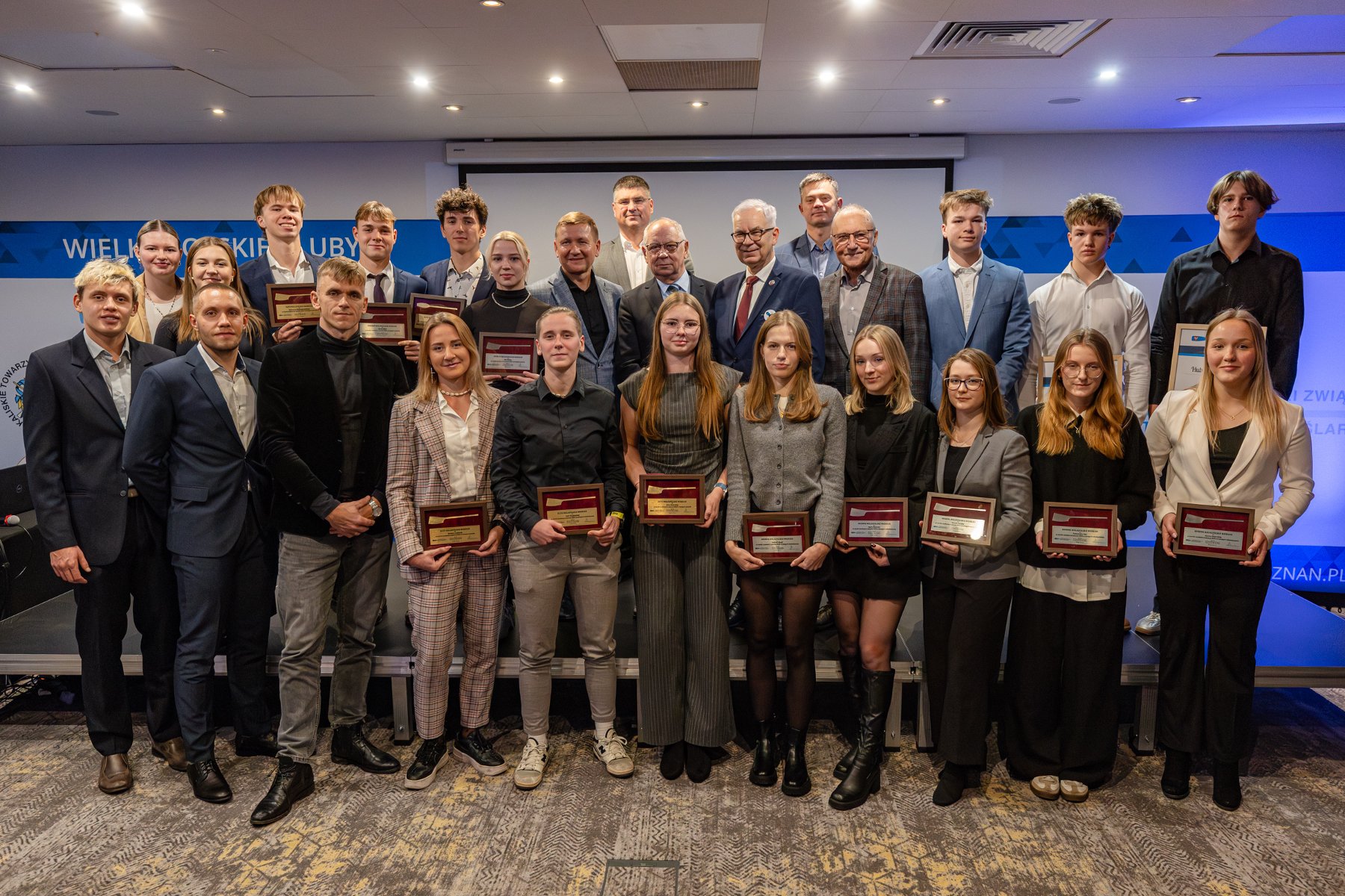 Podsumowanie sezonu wioślarskiego w Wielkopolsce, fot. Piotr Rychter - wszyscy wyróżnieni na wspólnym zdjęciu. Na tle sceny w trzech rzędziach stoją młode zawodniczki i zawodnicy z nagrodami w eleganckich strojach. Wśród nich są również działacze wioślarskiego środowiska sportowego