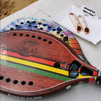 Na stole leżą dwie kolorowe paletki do tenisa plażowego.