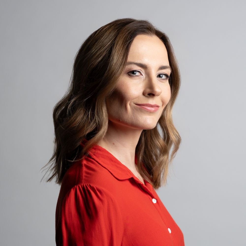 Katarzyna Wężyk, fot. Mikołaj Starzyński Profil uśmiechnietej młodej kobiety w czerwonej koszuli i rozpuszczonych włosach.