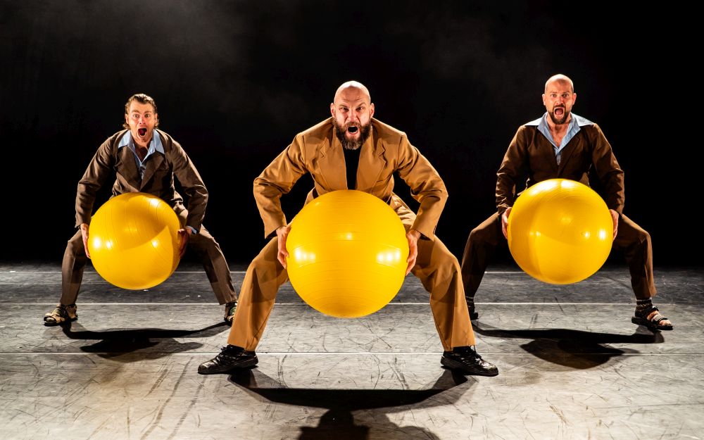 Spektakl "M.I.S. All Night Long", fot. Christoffer Brekne Trzech mężczyzn kuca z wielkimi, żółtymi piłkami.