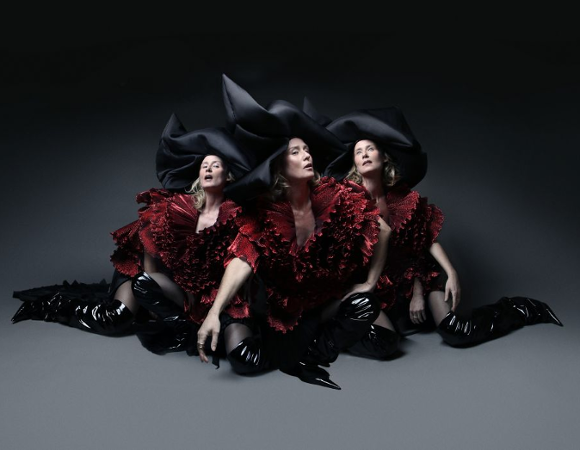 Roisin Murphy, fot. materiały prasowe Trzy kobiety siedzą na podłodze. Ubrane są w bordowe sukienki, czarne wysokie kozaki, na głowach mają czarne kapelusze. Ciemno-szare tło.