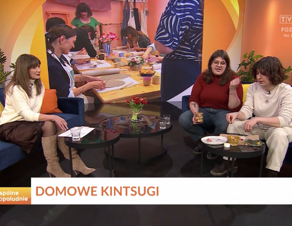 Trzy osoby siedzą na kanapach w studiu telewizyjnym, rozmawiając na temat aktualnych wydarzeń.