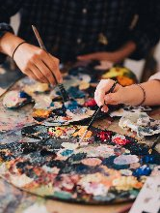 Dwie dłonie trzymające pędzle do malowania. Pędzle są maczane w farbie.