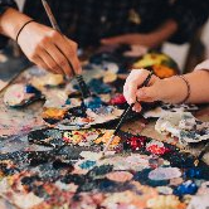 Dwie dłonie trzymające pędzle do malowania. Pędzle są maczane w farbie.