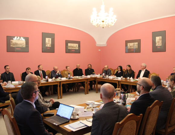 Wioczna cała sala Malinowa, na ścianach grafiki w ramkach. Przy długim, drewnianym stole w kształcie podkowy siedzą naukowcy i naukowczynie w uoczystych strojach. Na szczycie stołu jest prezydent Jaśkowiak.