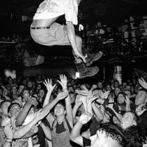 Czarno-białe zdjęcie zatłoczonego klubu, nad uczestników wyskakuje jeden z słuczaczy.