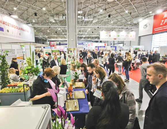 Wnętrze pawilonu targowego. Widać na nim stoiska handlowe i tłumy ludzi.