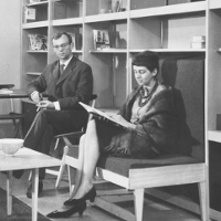 Kobieta i mężczyzna siedzą w pokoju, ona czyta książkę, on patrzy w bok. Zdjęcie czarno-białe.