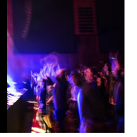Artystycznie rozmyte zdjęcie z zamkowego koncertu w Sali Wielkiej. Roztańczona publiczność przed zamkową sceną oświetloną kolorowym światłem.