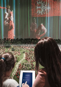 dwie osoby z interaktywnym tabletem przy makiecie Bitwy pod Grunwaldem